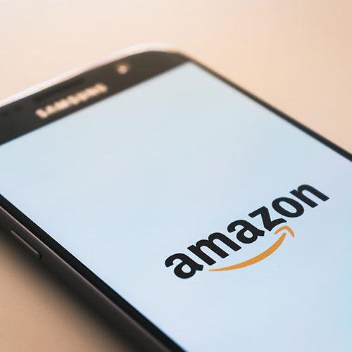 A simple closeup shot of a Samsung phone sitting on a beige table that is loading the amazon app on-screen
