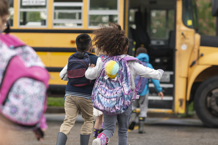 Group of children running excitedly toward open door of a school bus
